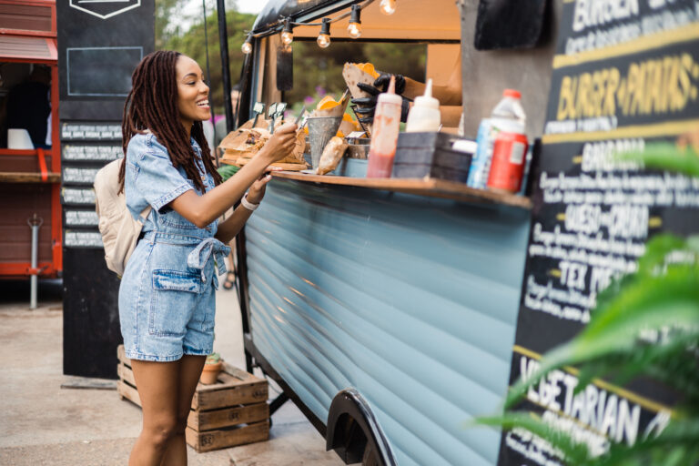 Beautiful young woman buying fast food at the food truck on the street